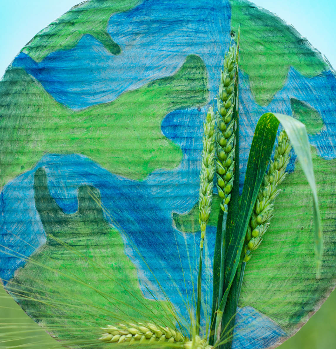 Teen girl holding planet and green spikelets of wheat in hands against green spring background. Earth day holiday concept. Protection and love of earth